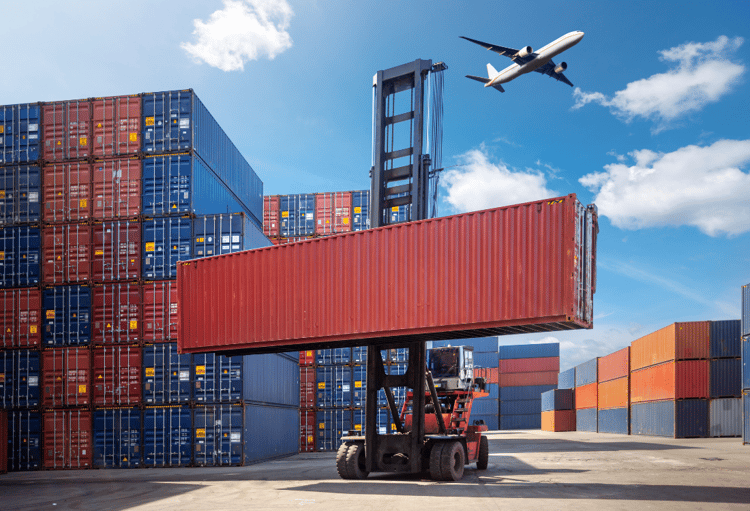 Forklift moving a shipping container at a busy port with an airplane flying above, symbolising global logistics in 2025.