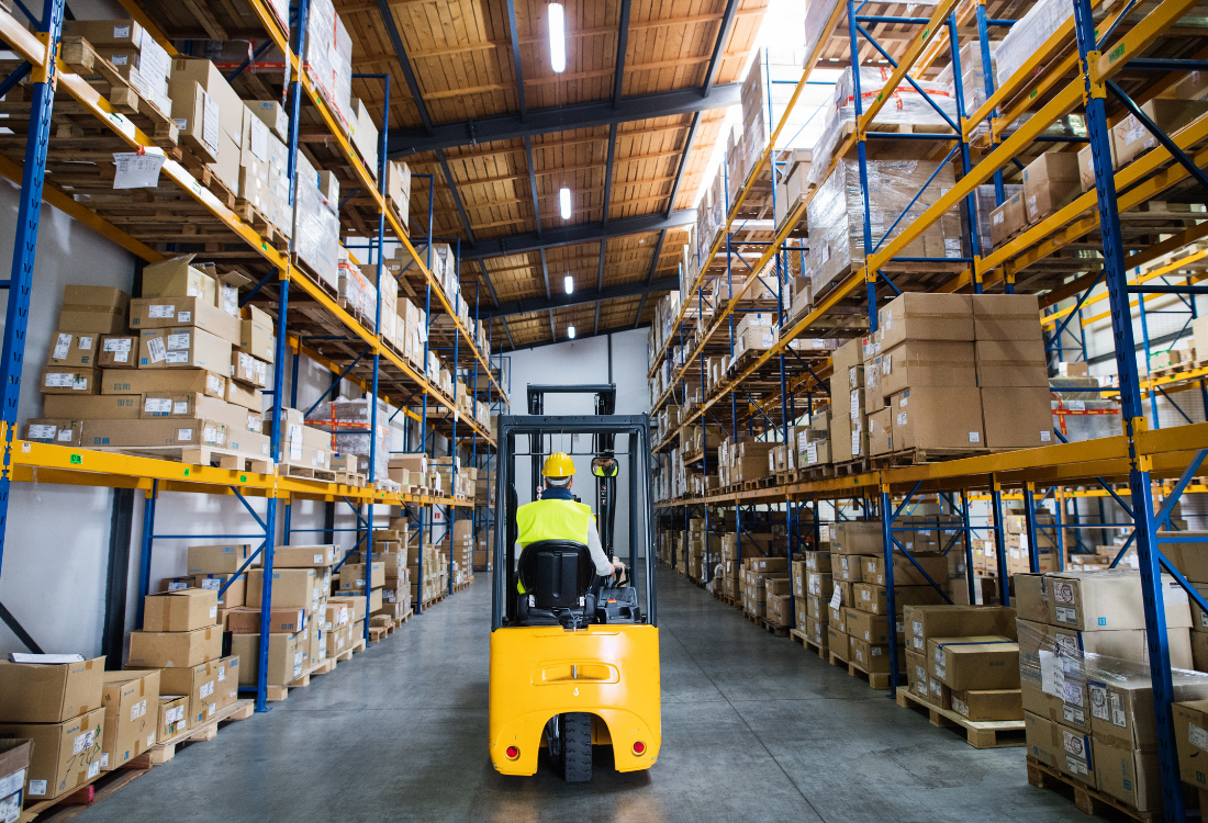 A warehouse worker operating a yellow forklift between tall racking aisles filled with boxes and pallets, representing efficient warehouse layout design and the balance between supplier and logistics consultant expertise.